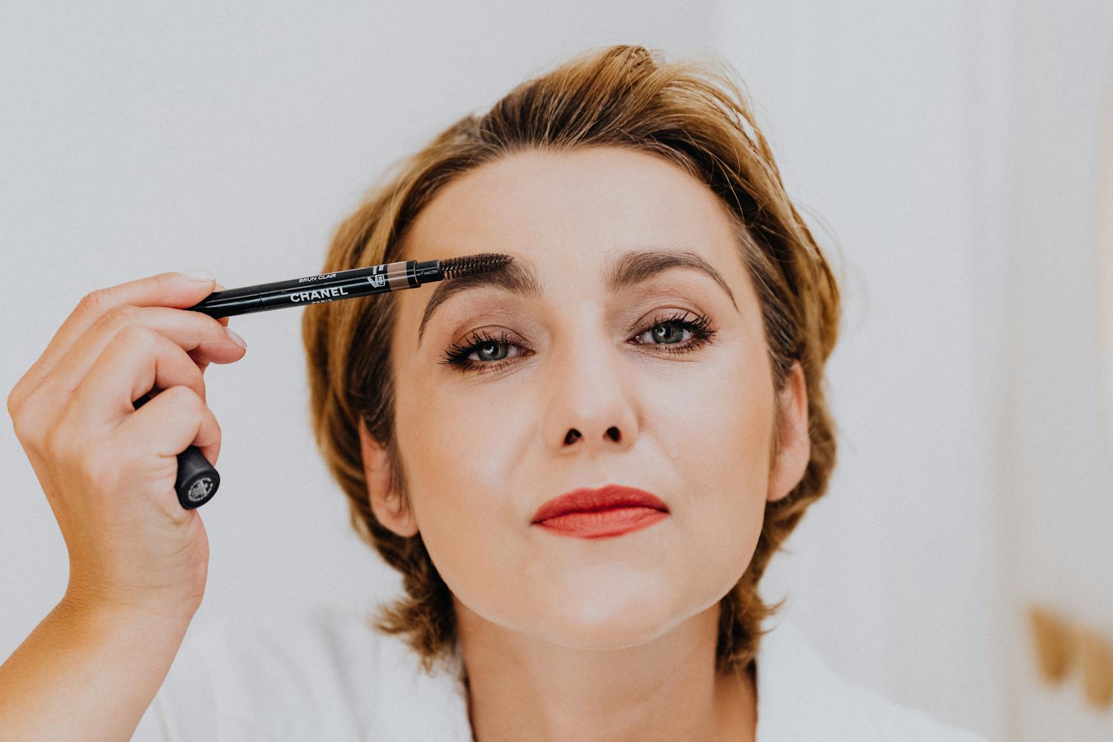 Portrait of a woman applying makeup with an eyebrow pencil, showcasing elegance.